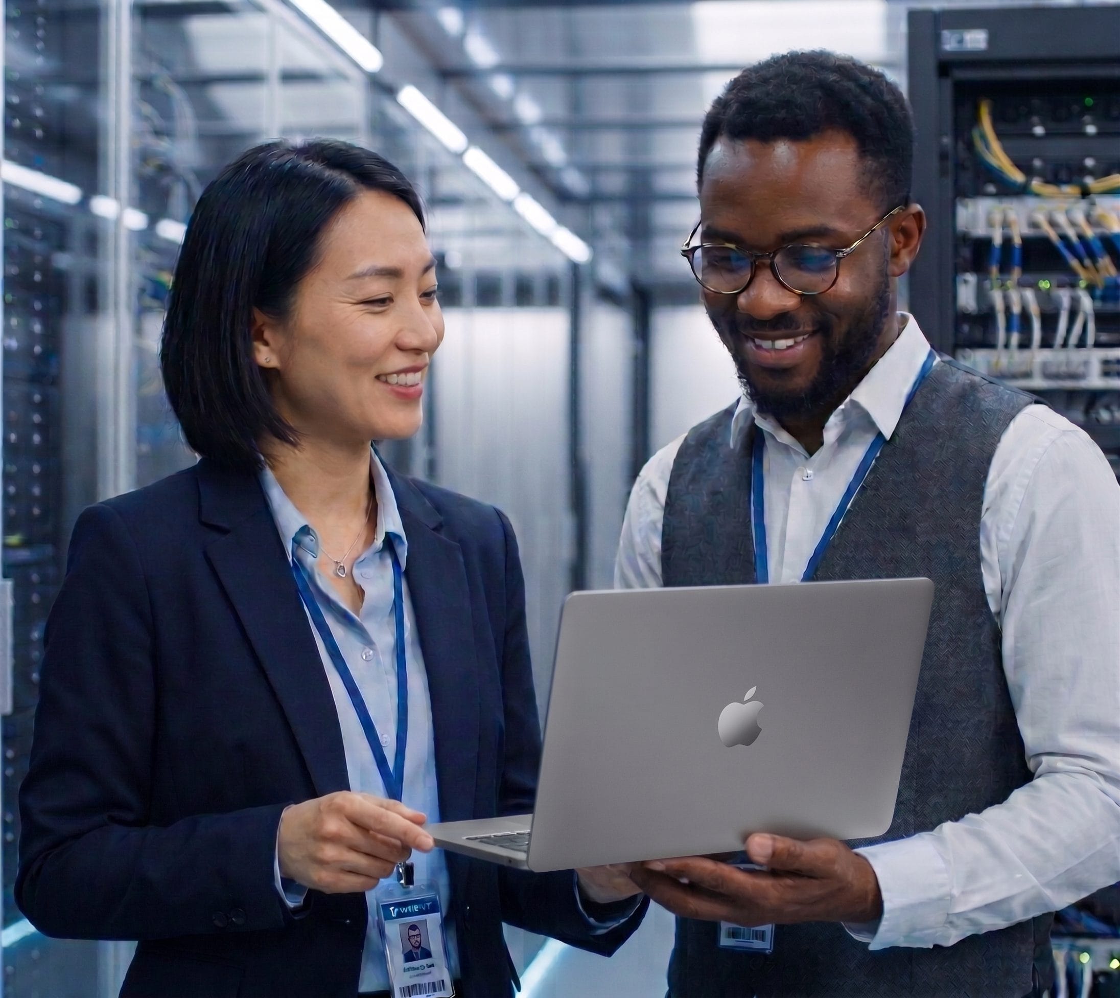 Man and woman in business attire smiling while looking at a laptop together in a data center server room